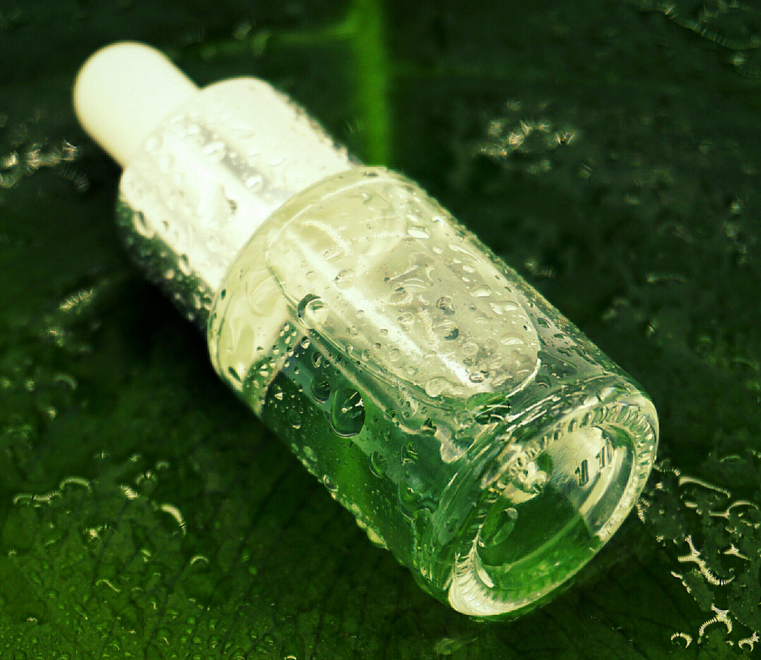Serumfläschchen mit Pipette auf der Seite auf einem grünen Blatt liegend voller Wassertröpfchen